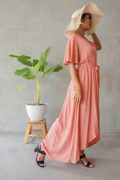 Woman in a dusty rose flutter-sleeve maxi dress standing beside a potted plant