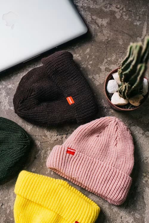 Ribbed knit beanies in charcoal, pink, yellow, and olive arranged on a stone surface