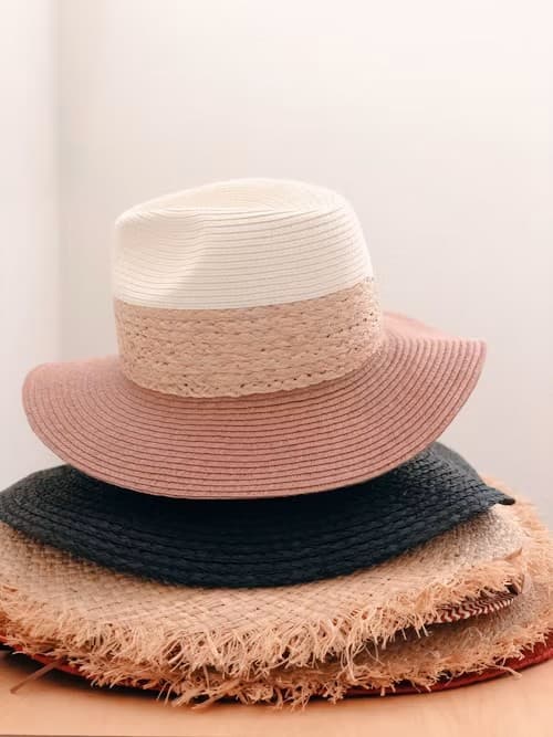 Stack of straw and raffia sun hats in cream, blush, and navy on a wooden surface