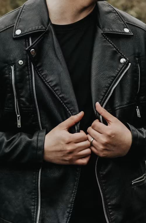 Young man wearing a tan shearling flight jacket in front of a dark urban building facade